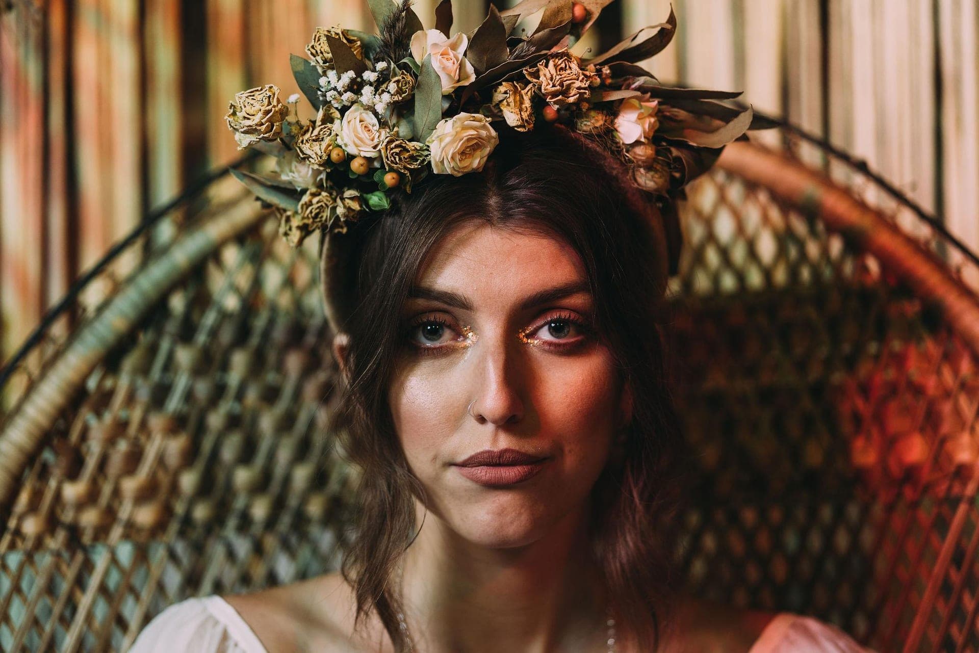 A bride in a dried-flower crown seated in a rattan peacock chair