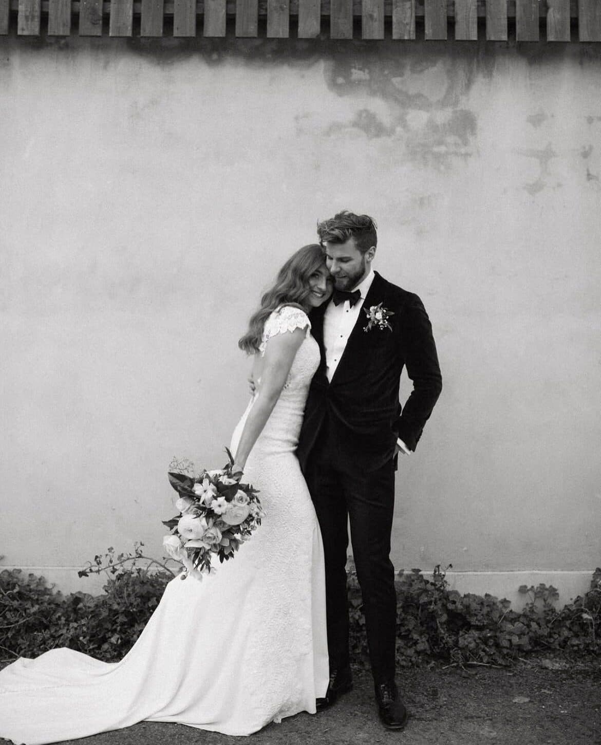 Black and white photo of a bride and groom leaning on a wall